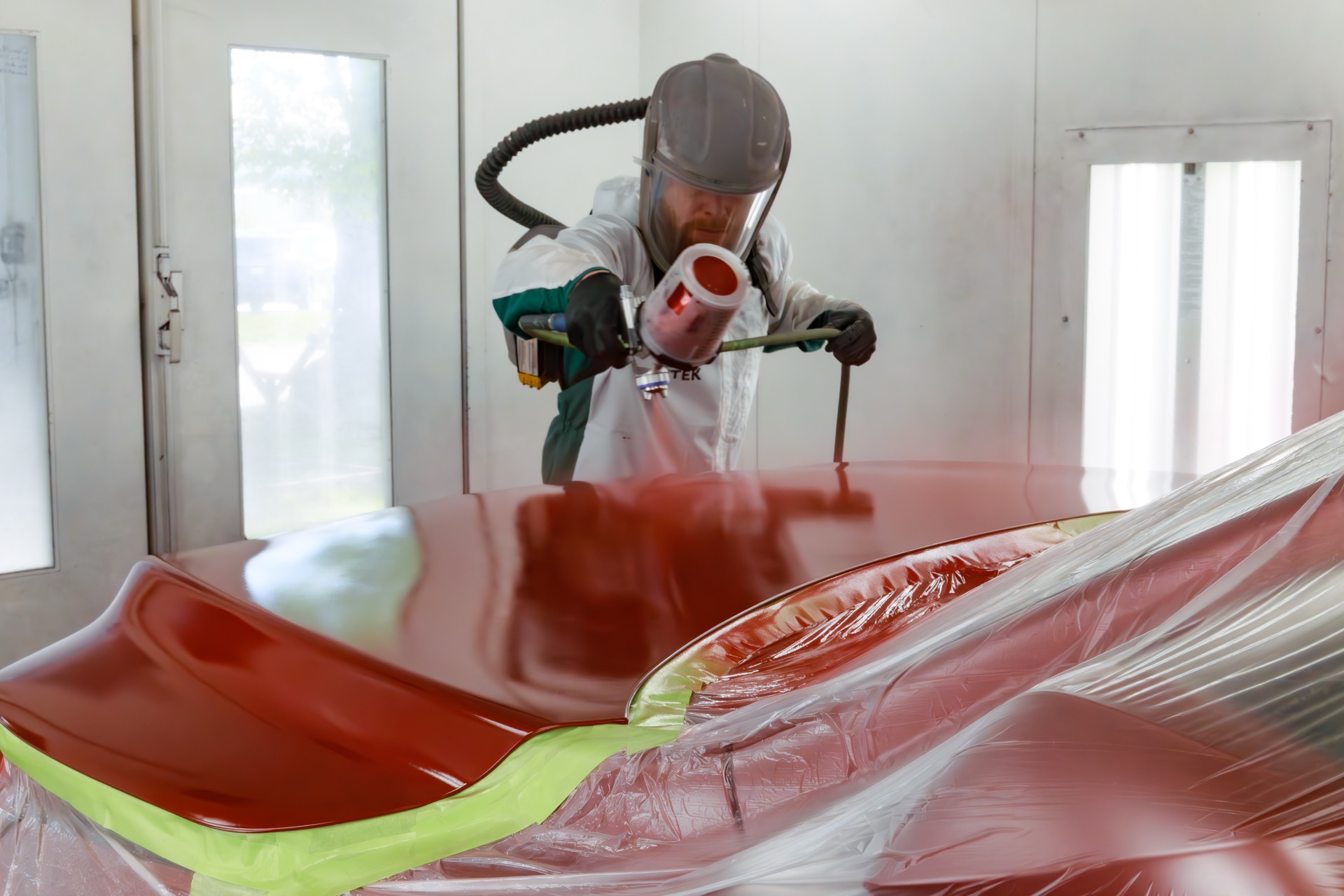 A Willis Collision painter applying a fresh basecoat inside the paint booth.